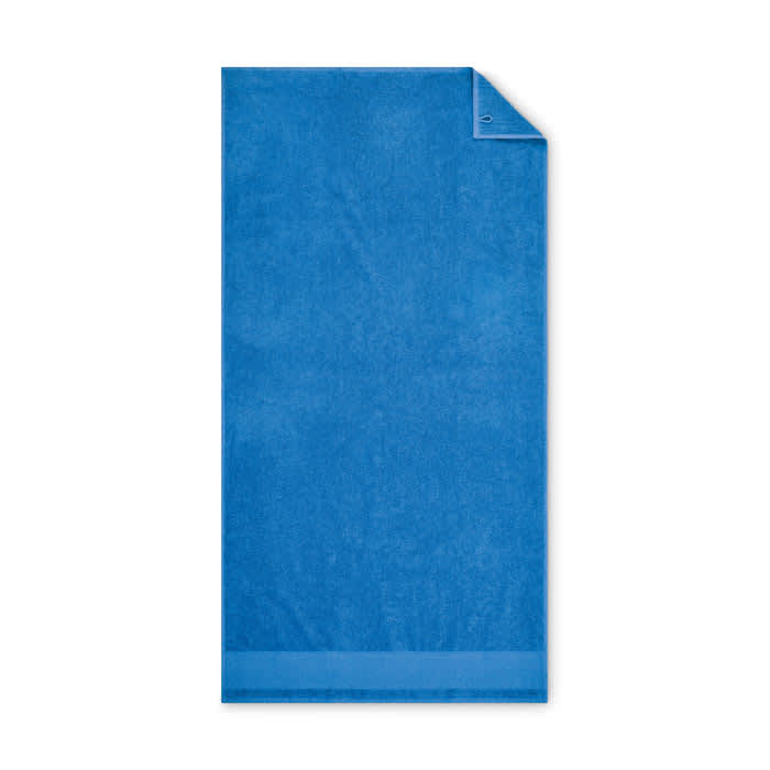 A blue towel featuring a corner tag and a soft, plush texture. It has a simple, solid design.