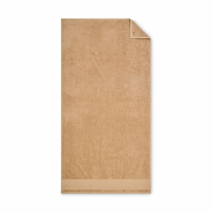 A bath towel in a soft beige colour, featuring a folded corner and a subtle texture. It includes a logo.
