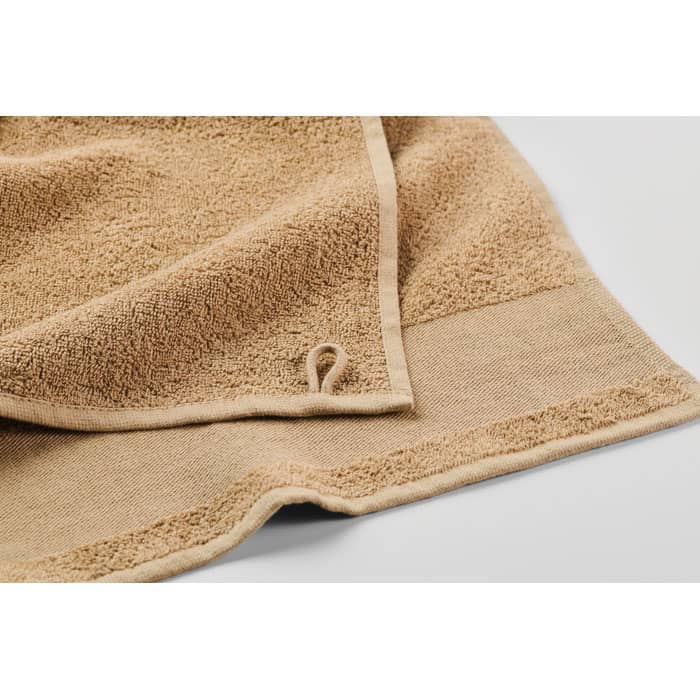 A towel in a soft sandy beige colour with a textured surface and a small loop for hanging.