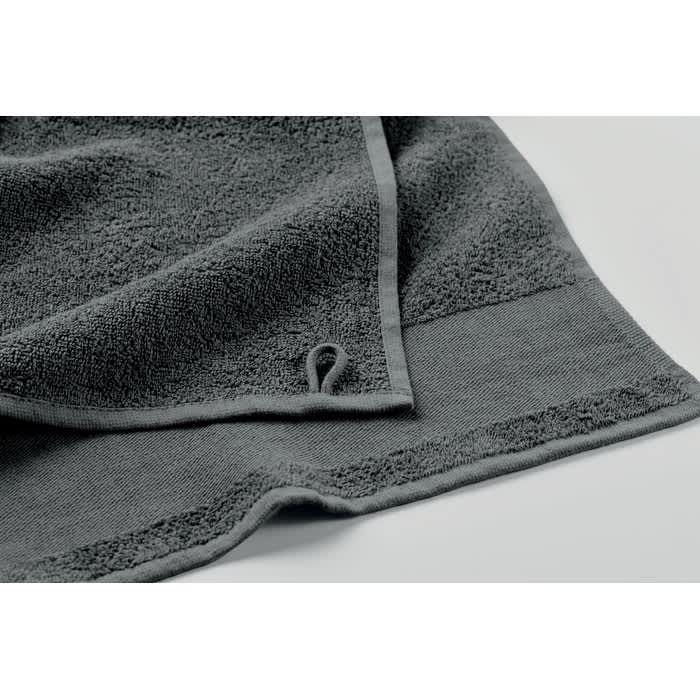 A grey bath towel with textured fabric and a hanging loop on the corner. It is neatly folded.