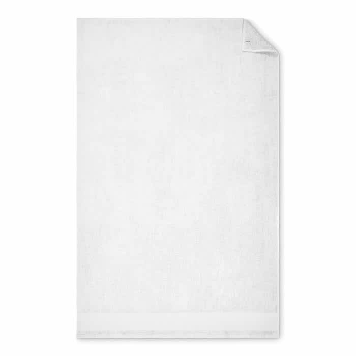 A white bath towel with a folded corner, featuring a subtle texture and an embroidered logo at the edge.