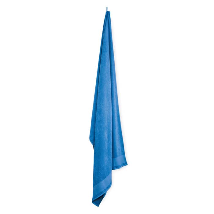 A blue towel hanging vertically, made of soft fabric with a hemmed edge. It has a simple, clean design.