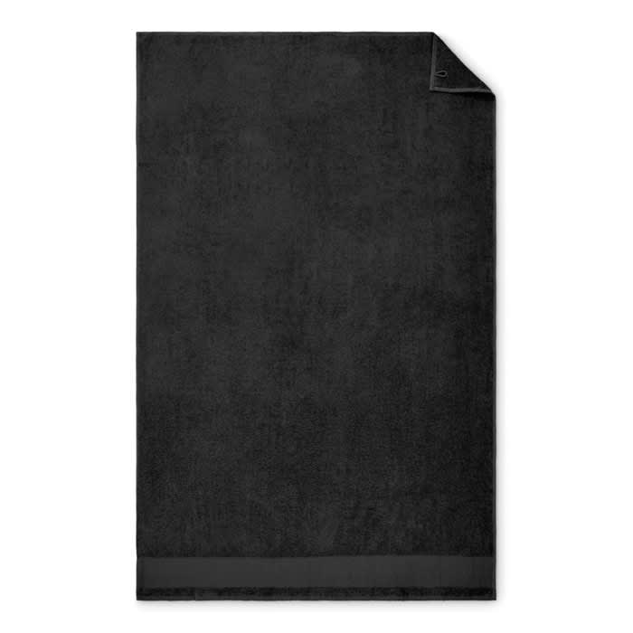 A black towel with a textured surface and a corner folded down, featuring a small logo.