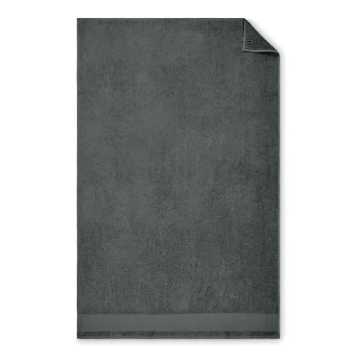 A dark grey bath towel with a textured finish and a folded corner, featuring a discreet logo.