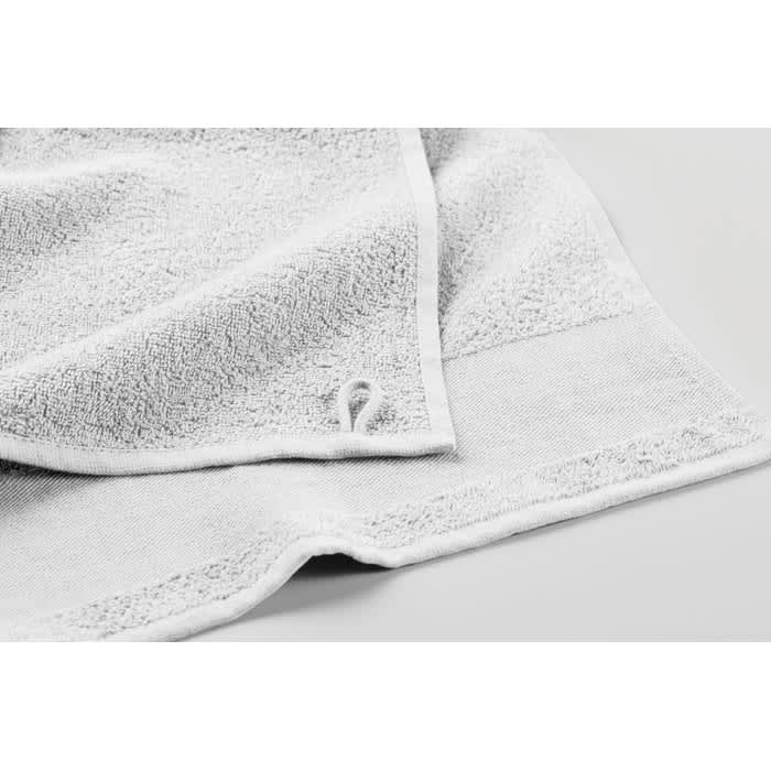 A white towel with a textured surface and a small logo on the edge, featuring a folded corner.