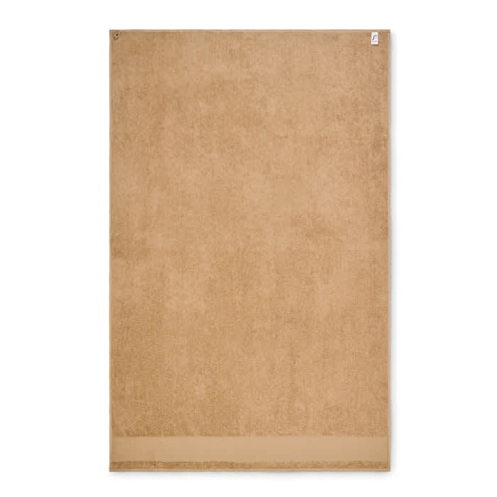 A bath towel in a sandy beige colour, featuring a soft texture and a simple design. It has a branding logo on one edge.