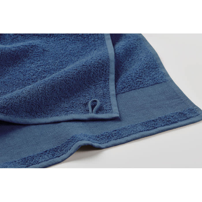 A blue towel with textured fabric and a hemmed edge, featuring a small loop for hanging.