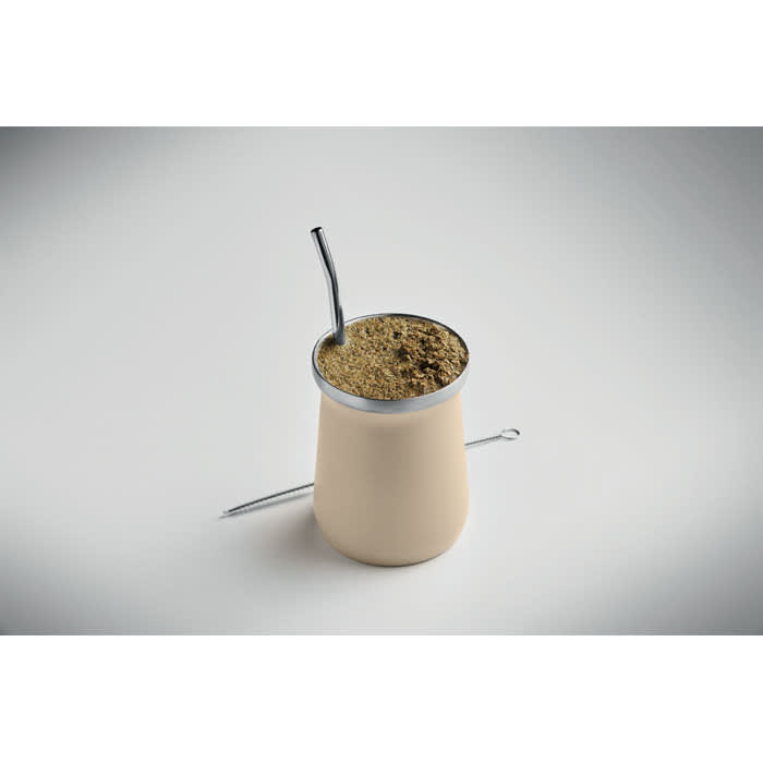 A drink bottle in a creamy beige colour with a metal straw and a layer of dried herb mix inside.