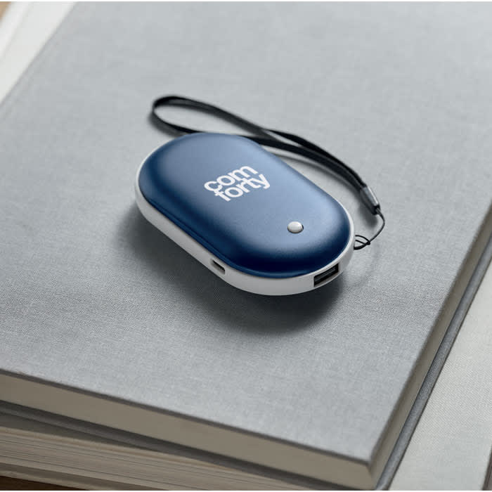A navy blue portable device with a white base, featuring a logo and a small strap, resting on a grey notebook.