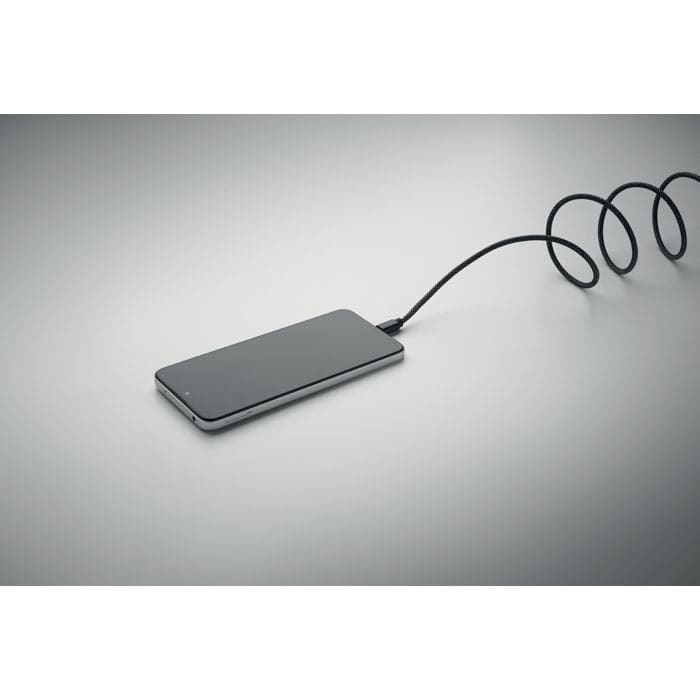 A power bank in sleek black, connected with a coiled charging cable on a grey surface.