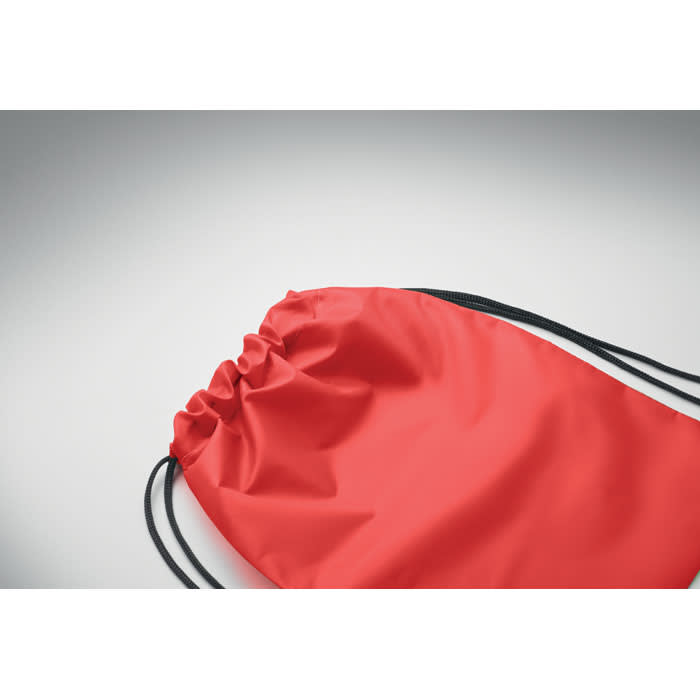 A red drawstring bag with black cords, featuring a smooth exterior and closed at the top.