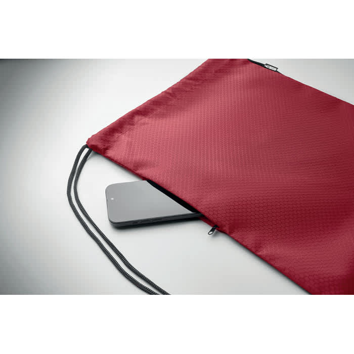 A maroon drawstring bag with a grey smartphone partially visible inside. The bag features a zipper closure.