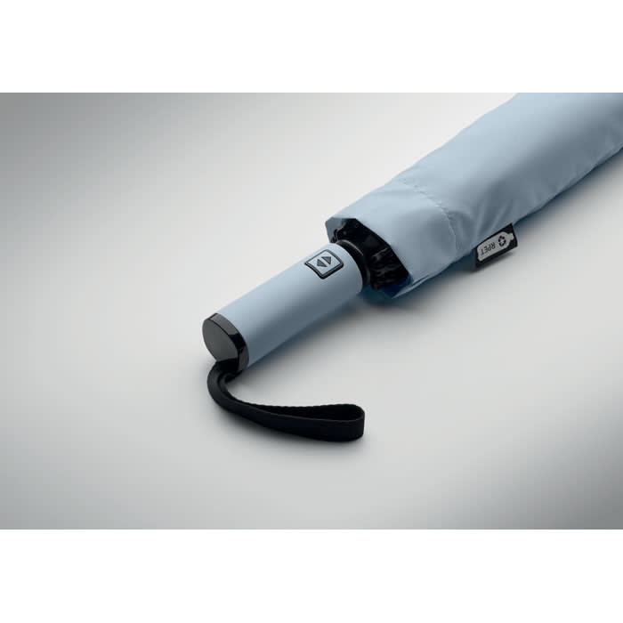 A light blue umbrella partially opened, featuring a sleek handle and a strap for holding. It has a branded logo on the side.
