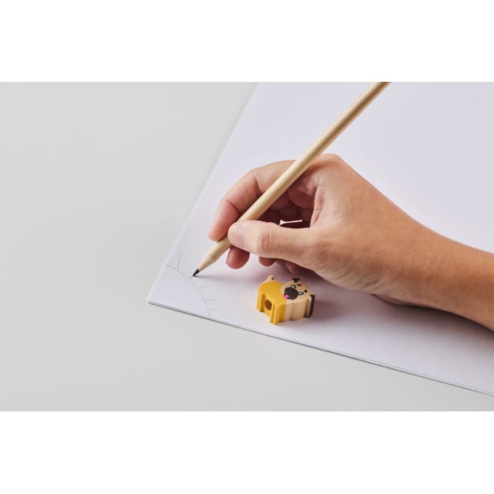 A hand holding a pencil draws on a white sheet of paper, next to a yellow pencil sharpener.