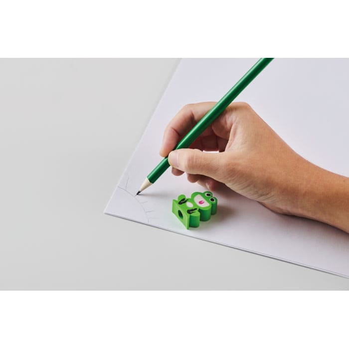 A hand holding a green pen draws on white paper beside a green pig-shaped eraser.