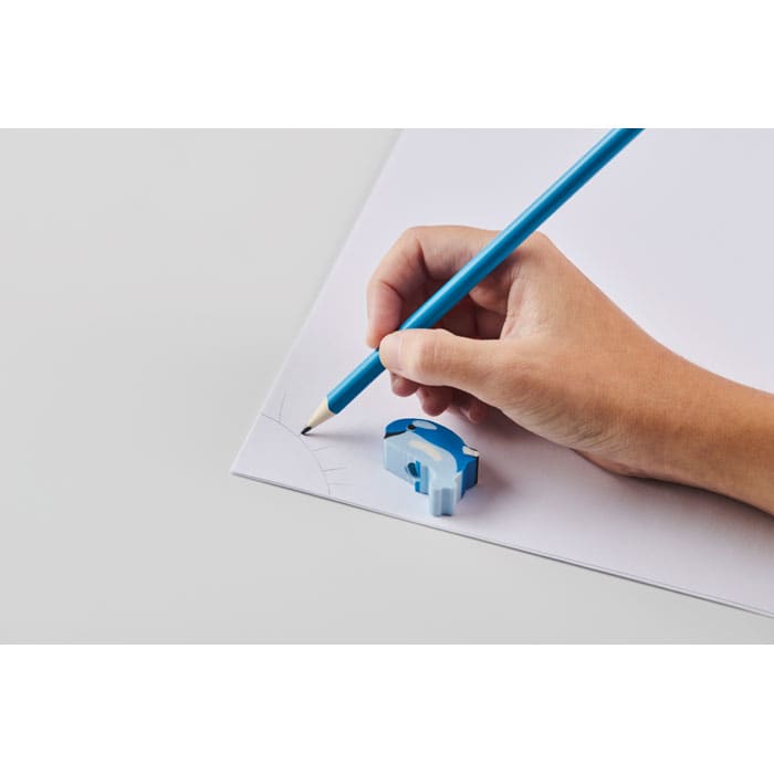 A hand holding a blue pencil is drawing on white paper next to a blue sharpener.