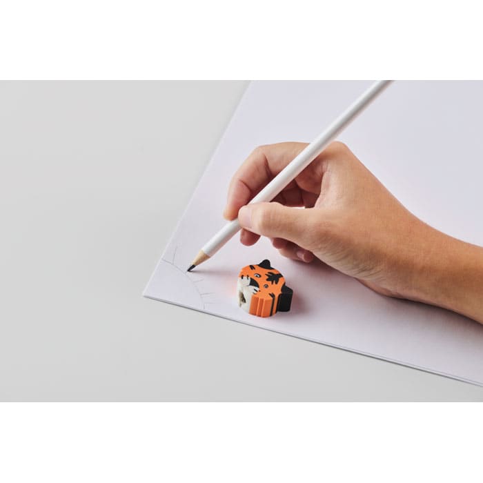 A hand holding a pencil draws on white paper, with an orange and black animal-shaped eraser nearby.