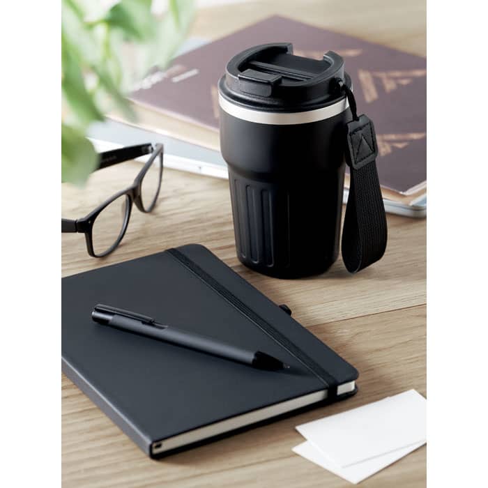 A drink bottle in black with a silver band, alongside a notebook, pen, glasses, and some business cards on a wooden surface.