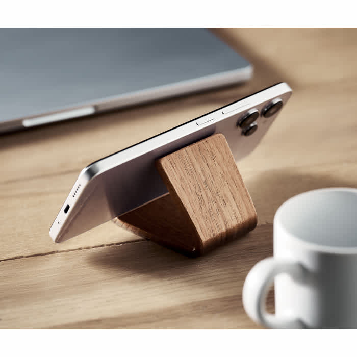 A wooden phone stand displaying a smartphone, set on a wooden surface next to a white mug.