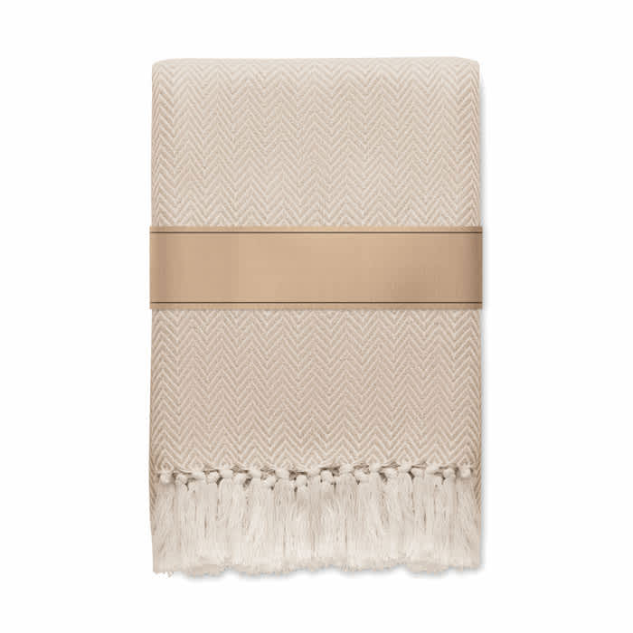 A woven blanket in a light beige colour with a herringbone pattern and decorative fringes at one end.