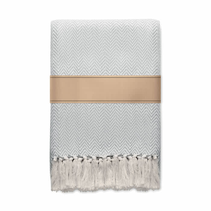 A blanket featuring a herringbone pattern in light grey, with decorative fringe and wrapped in a band.