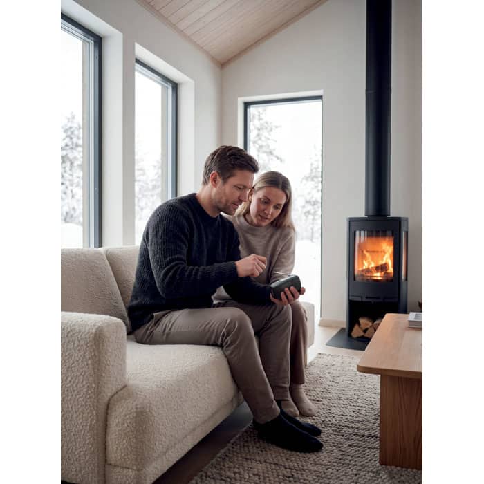 A couple sits close together on a light-coloured sofa, with a fireplace glowing in the background.