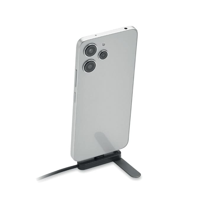 A smartphone in a sleek silver design, positioned upright on a small black stand, with a charging cable attached.