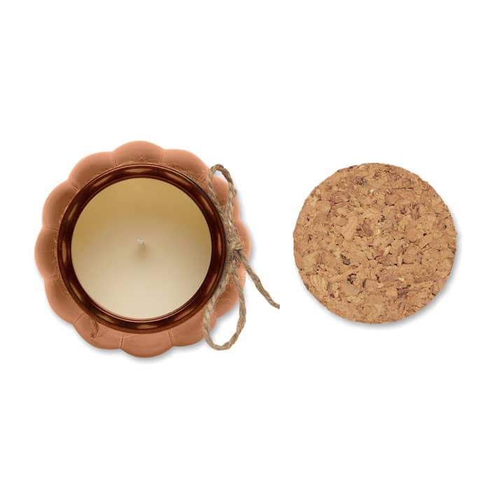 A candle in a terracotta pot with a cork lid. The pot has a scalloped edge and is beige in colour.