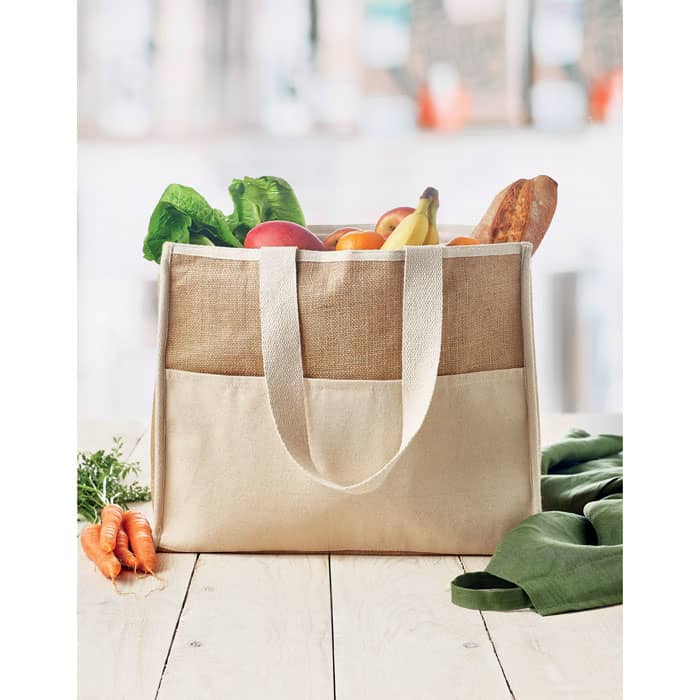 A tote bag in natural colours filled with fresh vegetables and fruits, featuring two sturdy handle straps.