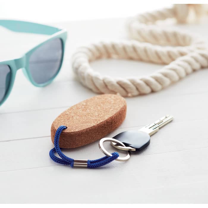 A cork keychain with a blue rope, keys attached, alongside sunglasses and a rope on a wooden surface.