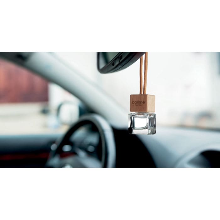 A wooden car air freshener hangs from the rear-view mirror, featuring a clear glass container filled with fragrance.