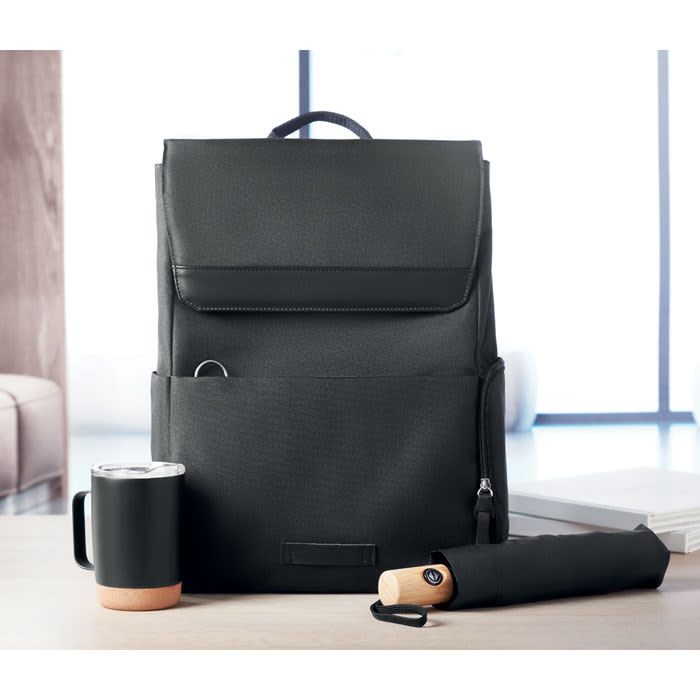 A black backpack with a front pocket, a black mug with a copper base, and a black umbrella on a table.