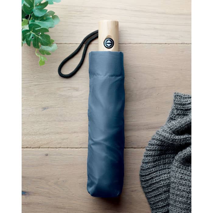 A folded umbrella in a dark blue sleeve with a wooden handle, accompanied by greenery and a knitted item.