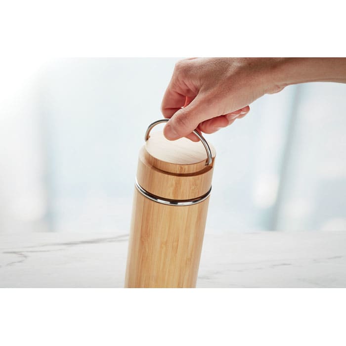 A drink bottle made of bamboo with a silver lid and a metal handle. The bottle has a smooth, natural finish.