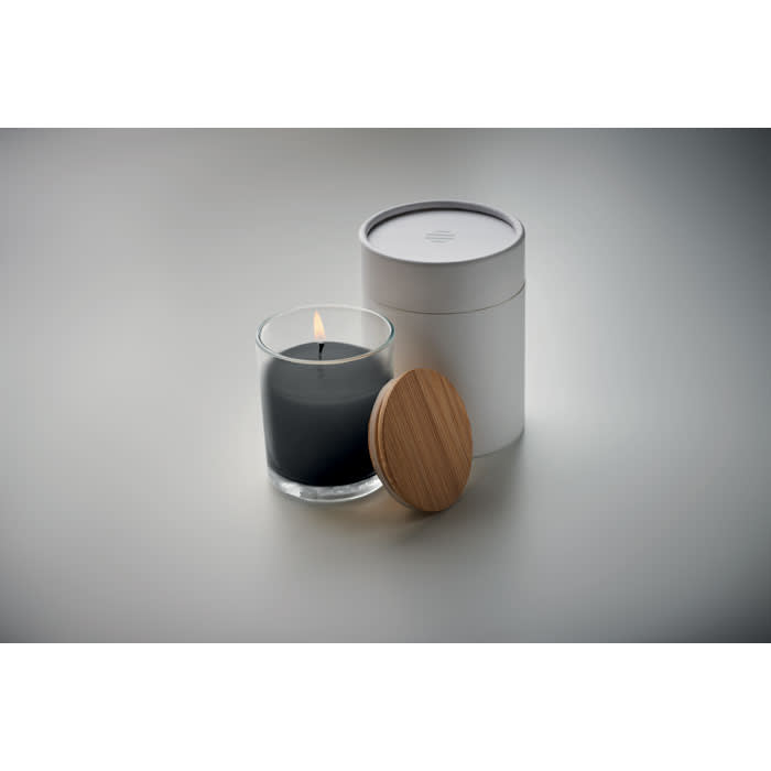 A candle with a grey wax inside a glass holder, accompanied by a white container and a wooden lid.