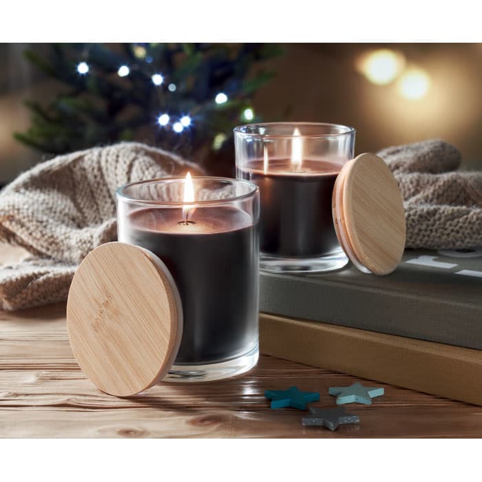 A set of two candles with black wax, glass containers, and bamboo lids, placed on a wooden surface with a cozy background.