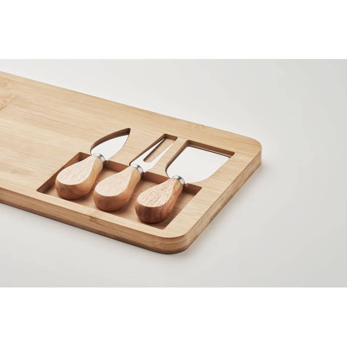 A bamboo serving board with three wooden-handled cheese knives displayed on it. The board has a minimalist design.
