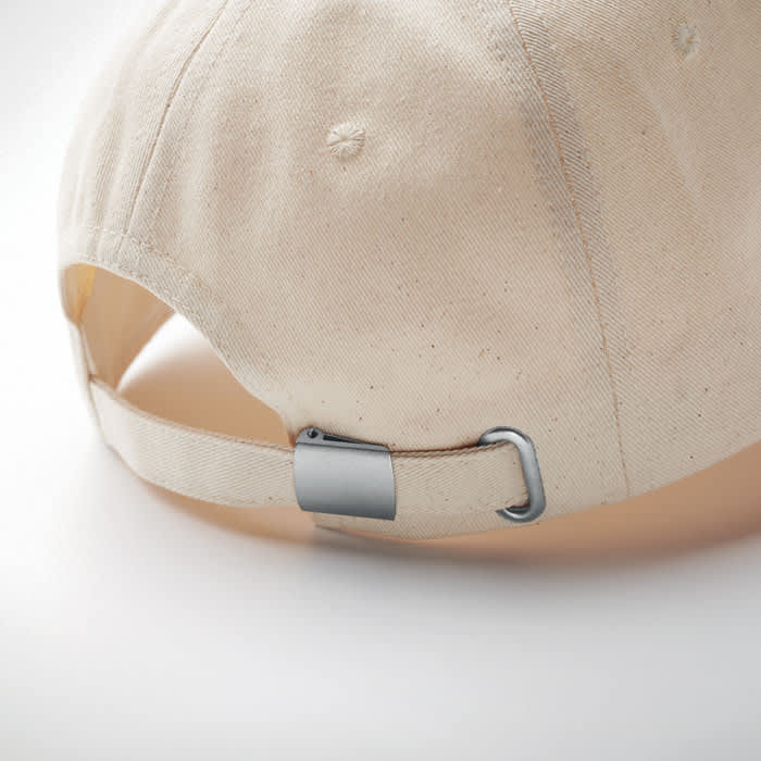 A cap in natural beige fabric with a metal adjustable strap at the back and a logo on the side.