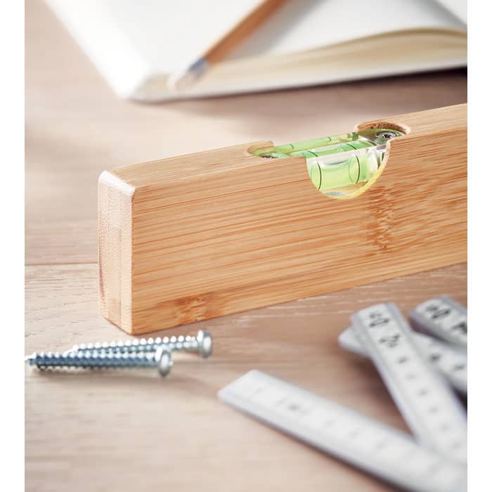 A wooden level with a green vial sits on a work surface alongside screws and measuring tapes.