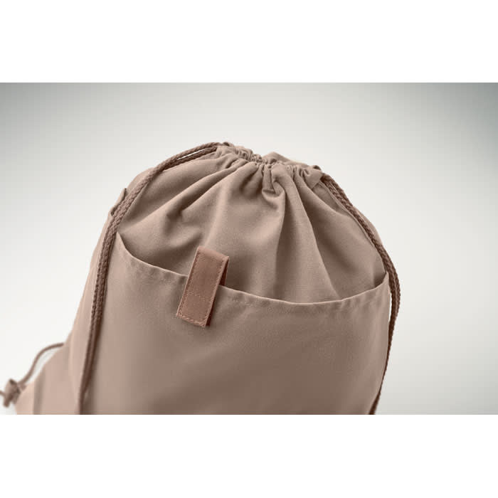 A beige drawstring bag with a gathered top and a small pocket on the side, featuring a logo.