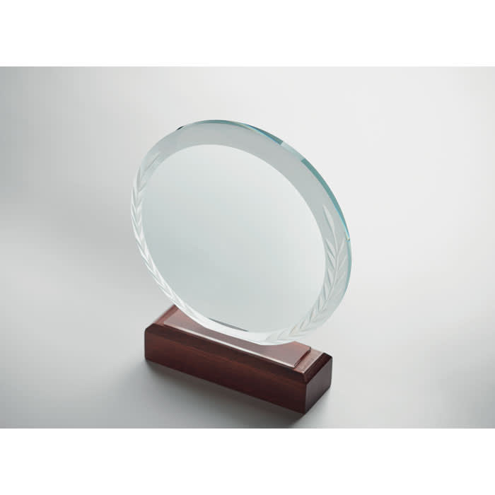 A circular crystal award with a clear surface, mounted on a wooden base. The edge features a subtle engraved pattern.