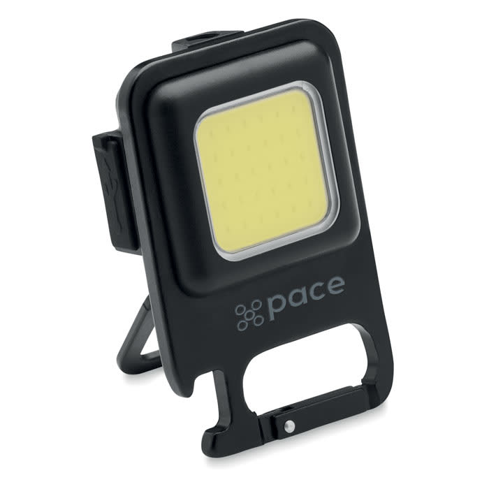 A portable LED light in black with a square yellow light panel, featuring a stand and a clip for easy attachment.