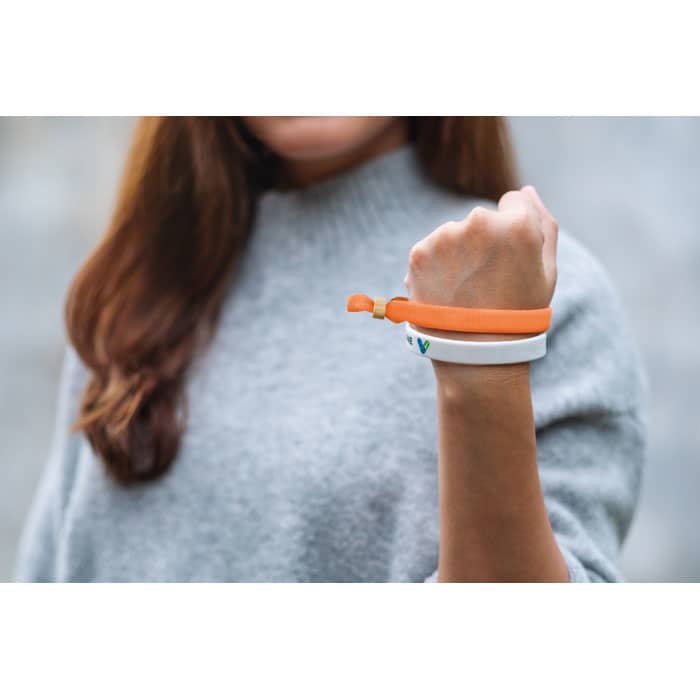 A wristband featuring an orange and white design, worn on a person's wrist, showcasing a logo.