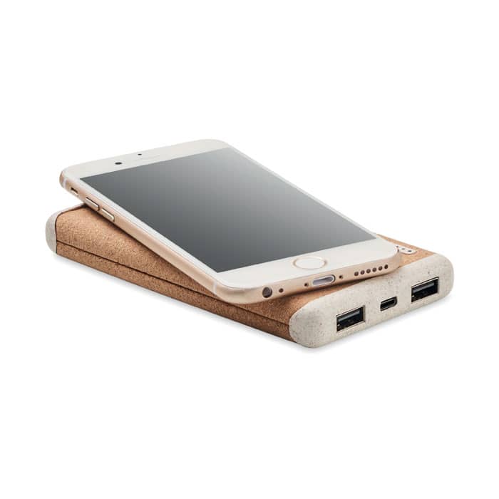 A power bank with a cork texture, featuring two USB ports, with a smartphone resting on top.