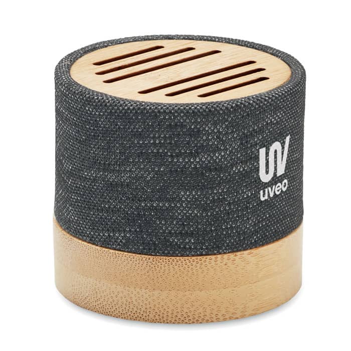 A round speaker in dark grey fabric with a wooden base and slotted top, featuring a logo.