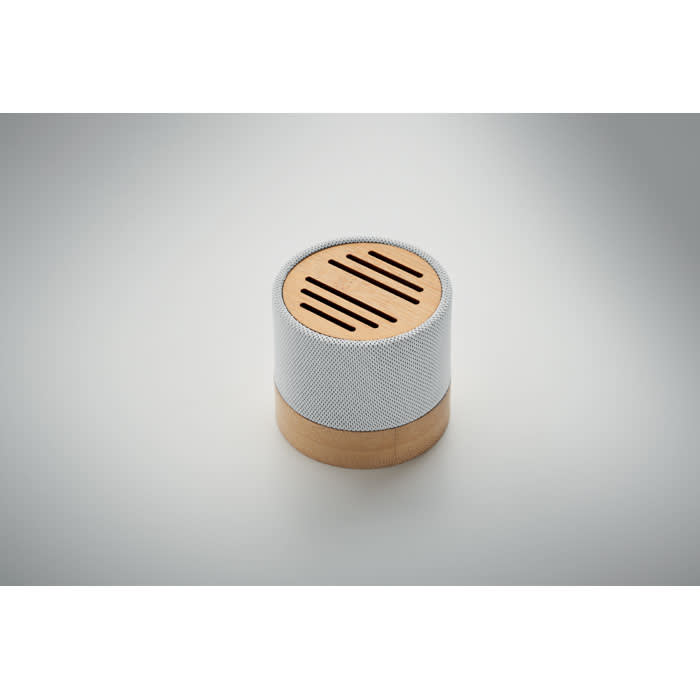 A small round speaker featuring a fabric exterior in grey and a wooden base. It has a slotted top design.