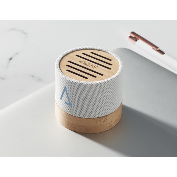 A portable speaker featuring a white fabric cover and a wooden base, with a logo on the front.