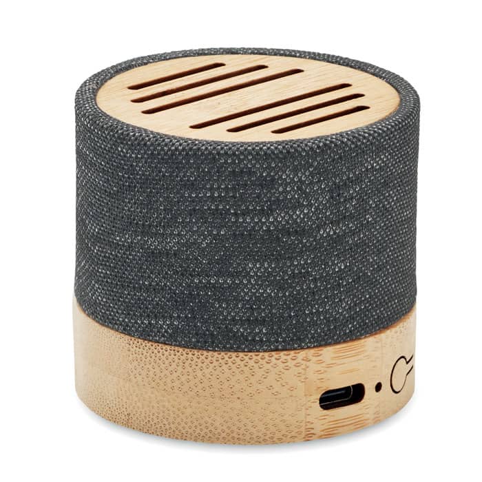 A round speaker featuring a textured grey fabric exterior and a bamboo base, with visible speaker vents and a charging port.