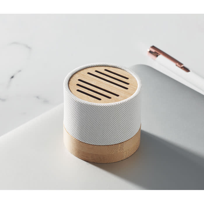 A portable speaker with a white mesh exterior and a wooden base, featuring a slotted top design.