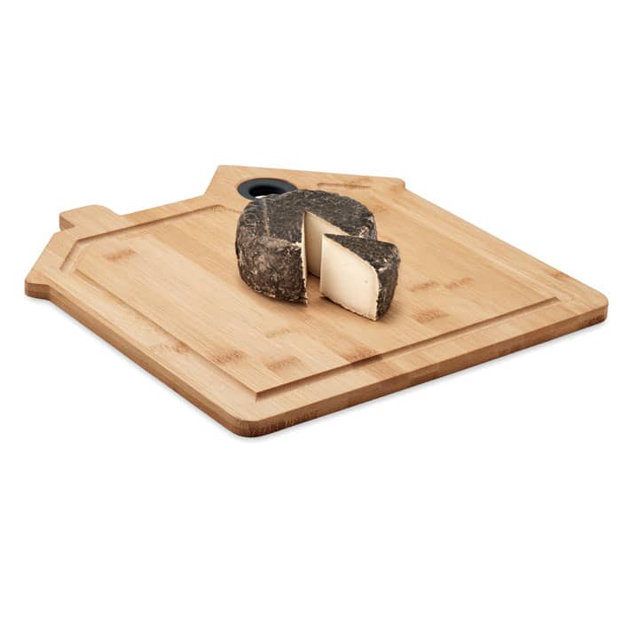 A cutting board shaped like a house, featuring a wedge of dark cheese, set on a light wooden surface.